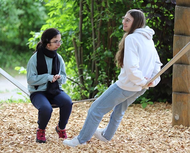 Schuelerinnen der foerderschule auf spielplatz sitzend auf seil