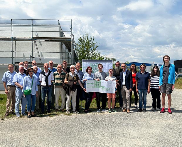 Circa 20 Menschen auf einem Gruppenfoto die einen Bau und Landchaftsplan hochhalten