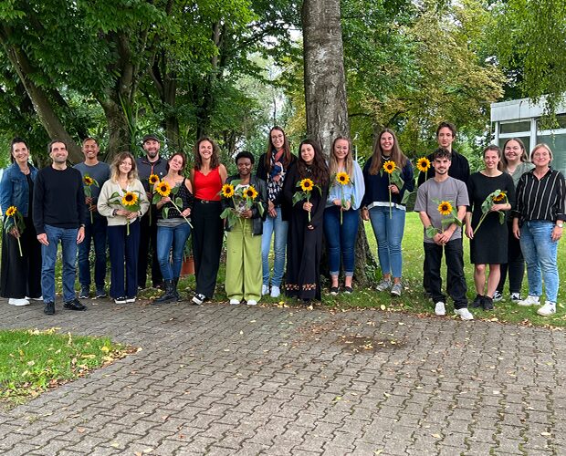 Eine Gruppe von jungen Erwachsenen und Jugendlichen mit Sonnenblumen vor grünen Laubbäumen
