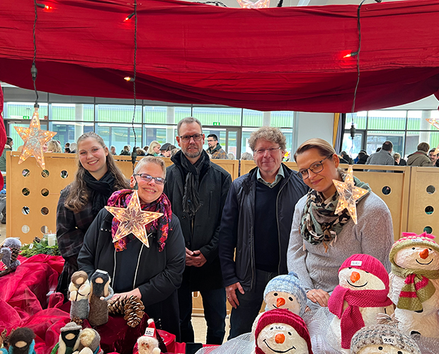 Zwei Männer und drei Frauen an einem Indoor Weihnachtstand mit Rotem Baldachin und Sternen. Im Vodergrund sind Weihnachsmänner zu sehen