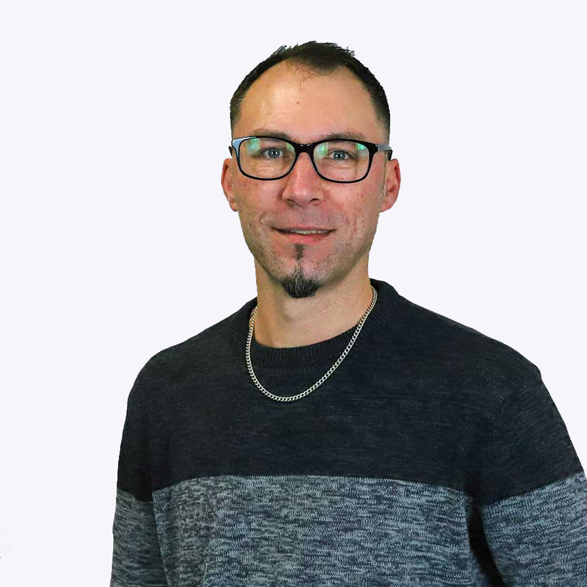 Eine Herr mit kurzen dunklen Haaren und blauen Augen, trägt eine Brille, ein schwarz-grauen Pullover. Er lächelt. Es handelt sich um ein Portrait.