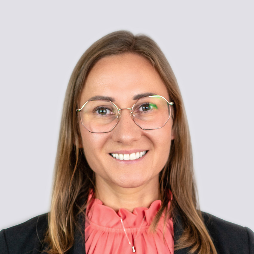 Frau mit Dunkelblondem Haaren. Sie lächelt und trägt eine Brille. Sie trägt einen dunklen Blaser mit einer hellen Bluse.